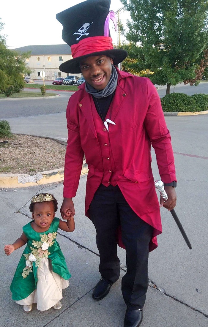 Man and child in clever Halloween costumes, featuring a top hat and princess dress, posing outdoors on a sidewalk.