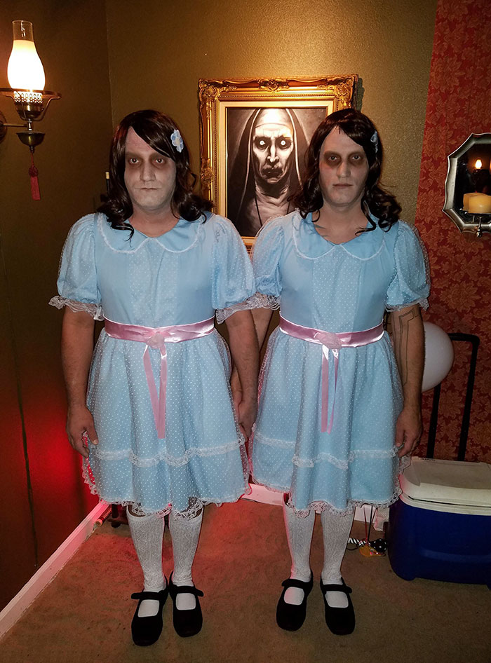 Two people dressed in clever Halloween costumes as creepy twins in blue dresses with black wigs and white stockings.