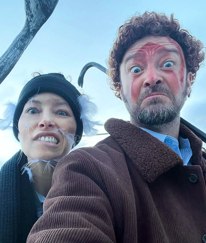 Two people in clever Halloween costumes with face paint and creative accessories, posing for a selfie outdoors.