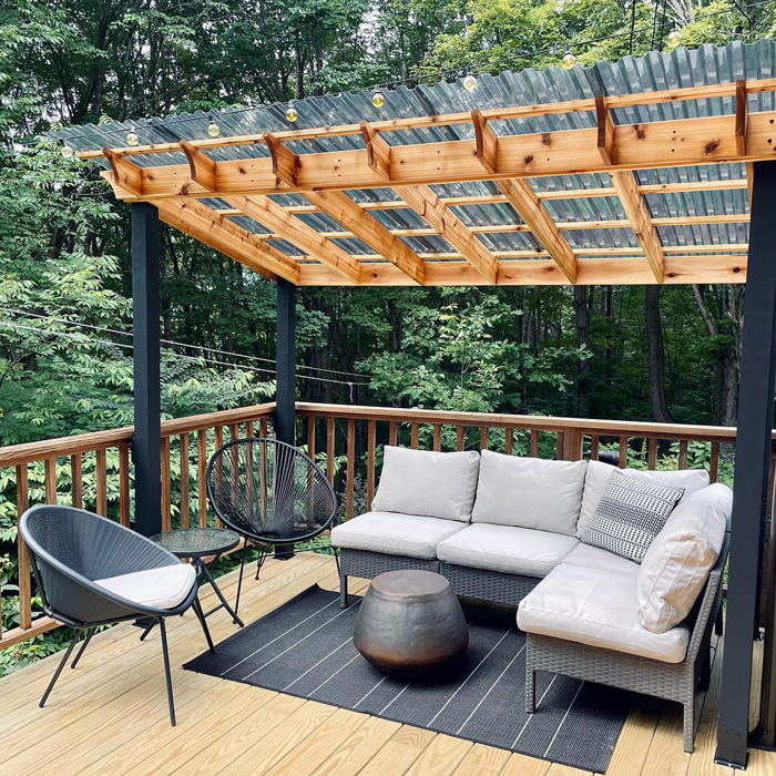 Backyard deck with covered pergola and grey furniture creating a creative outdoor seating area surrounded by trees