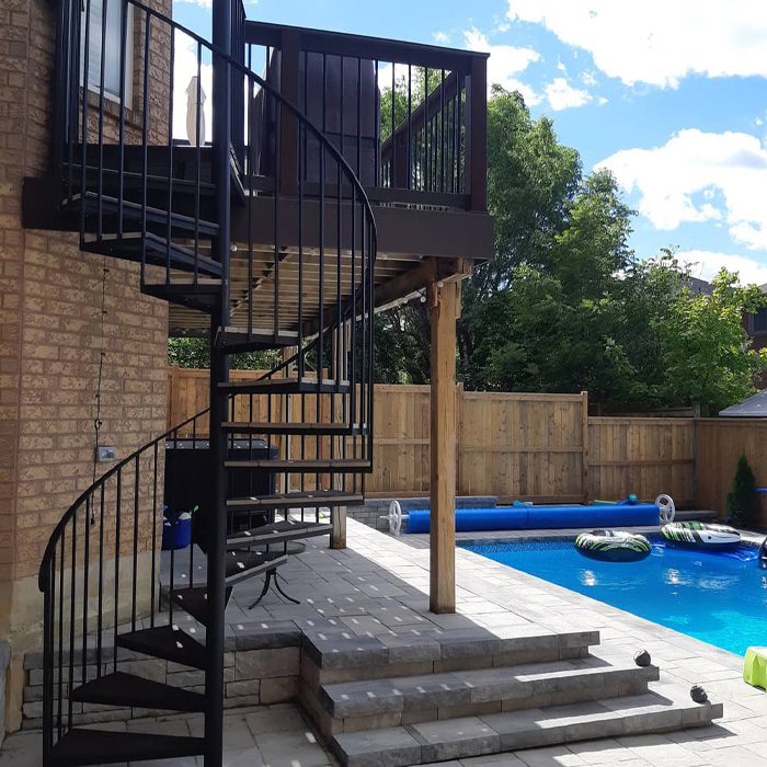 Spiral staircase deck design next to swimming pool in backyard showcasing creative backyard deck ideas outdoors.