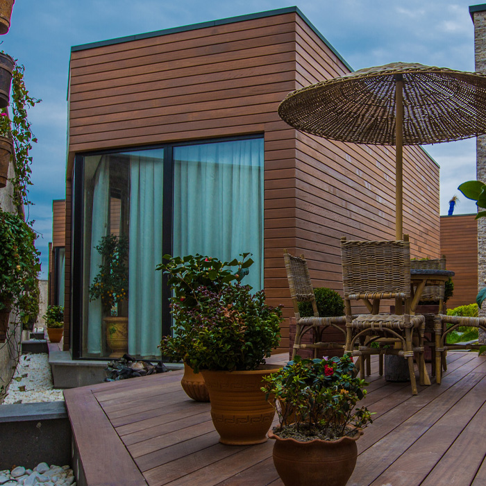 Modern house exterior featuring a wooden backyard deck with potted plants and wicker furniture enhancing outdoor living space.