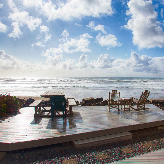 Wooden backyard deck with furniture overlooking ocean waves on a sunny beach showcasing creative backyard deck ideas.