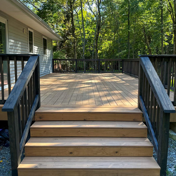 Raised backyard deck with wooden stairs and black railings surrounded by trees, showcasing creative backyard deck ideas.
