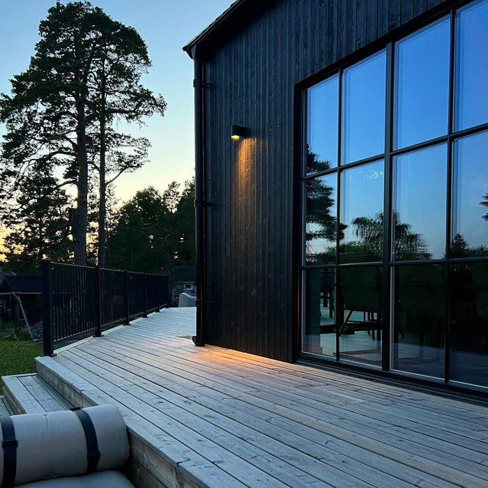 Spacious backyard deck wrapping around the house with outdoor lighting and large windows reflecting trees at dusk