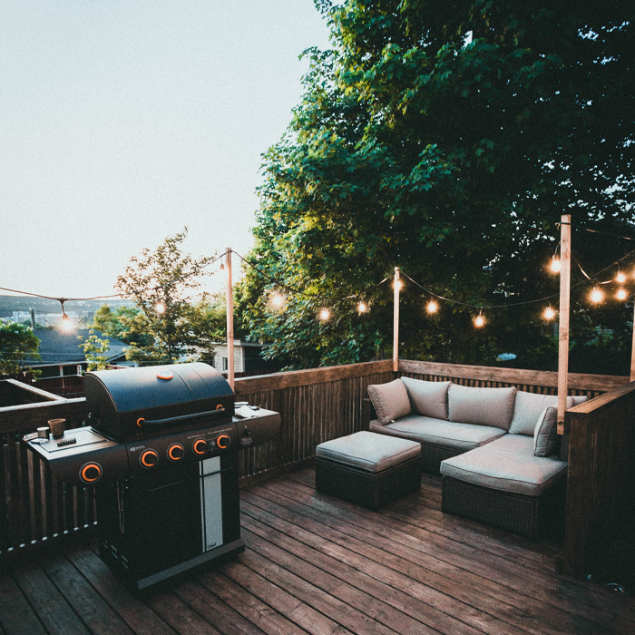 Black grill and cozy seating on a wooden backyard deck with string lights creating a warm outdoor ambiance.