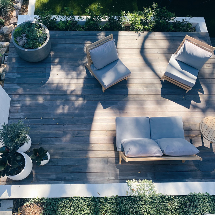 Wooden outdoor furniture with cushions and plants on a backyard deck showcasing creative backyard deck ideas.