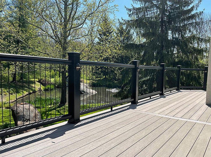 Classic black deck railing on a wooden porch overlooking a lush green landscape with trees and a small stream