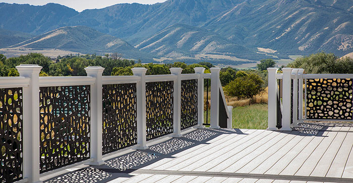 Ornament deck railing with black patterned panels and white posts enhancing outdoor deck design against mountain backdrop