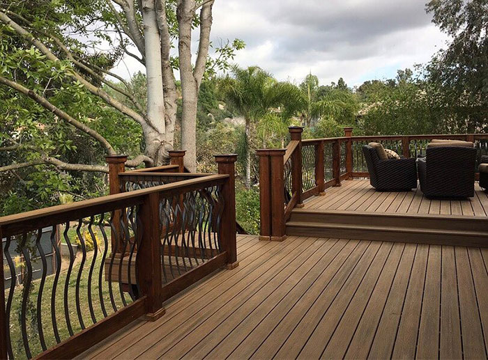 Wooden deck featuring arced black metal deck railings surrounded by trees and outdoor seating area.