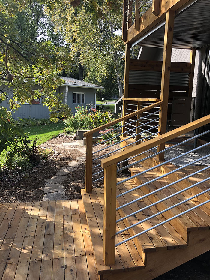 Wooden deck railing with metal horizontal bars in different colors enhancing modern deck railing ideas outdoors.