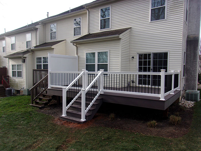 White and black deck railing design with stairs near a house, showcasing modern deck railing ideas for exterior spaces.