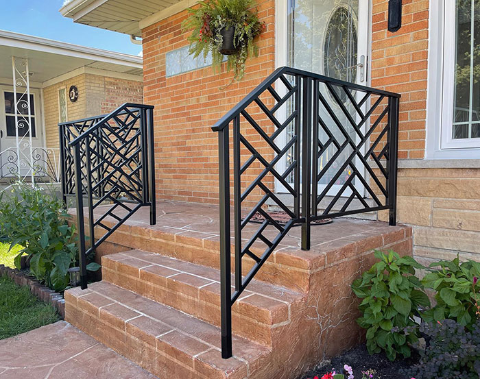 Black patterned metal deck railing with geometric design installed on brick steps enhancing exterior appearance.
