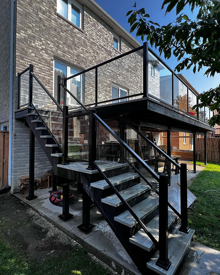 Modern multi-panel glass deck railing with black frames enhancing exterior design and safety on outdoor stairs and balcony.