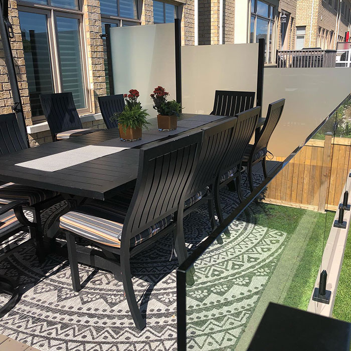 Patio with frosted glass deck railing and black outdoor dining table with chairs on patterned rug.