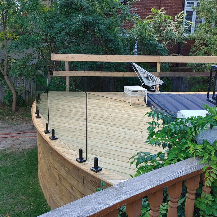Curved wooden deck with sleek single-panel glass deck railing design for a modern exterior look.
