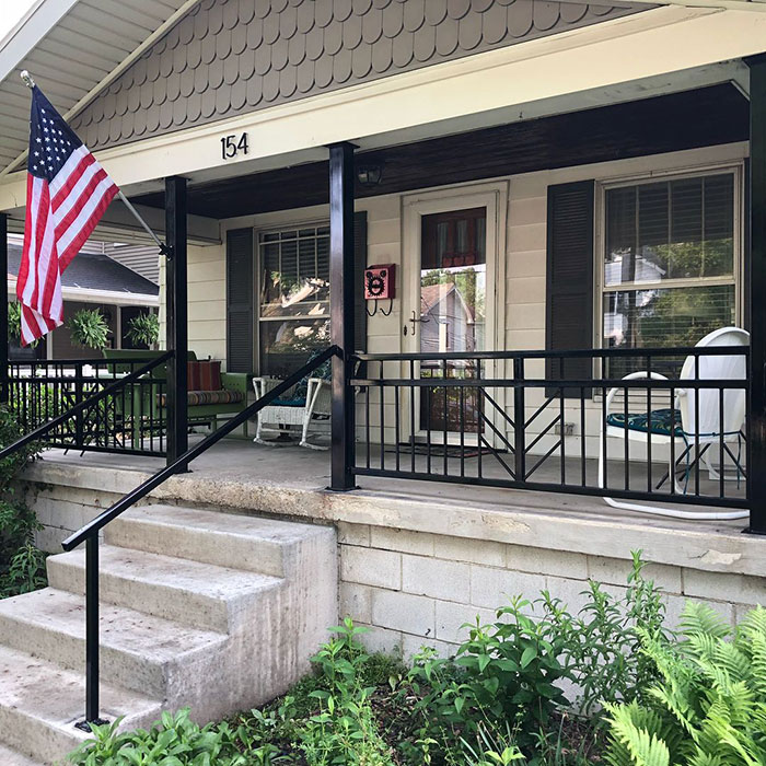 Black arrowhead deck railing design enhancing a house porch exterior with steps and nearby greenery.