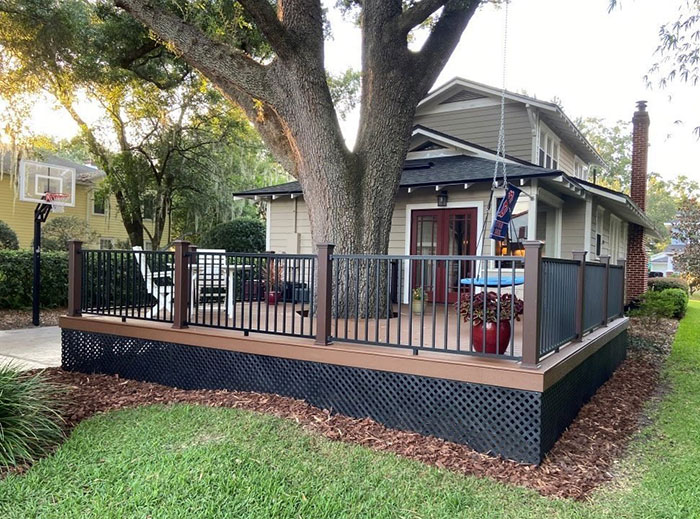 Wooden and metal deck railings surrounding a raised deck area near a house with outdoor seating and greenery.