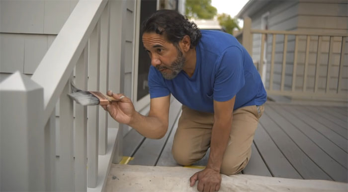 Man carefully painting white deck railing, enhancing outdoor space with creative deck railing ideas and designs.
