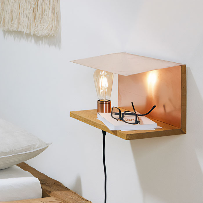 Wood and brass modern floating nightstand with built-in light holding books and glasses by a white bedroom wall