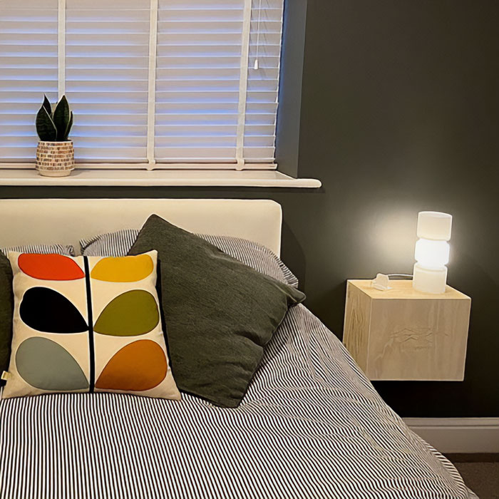 Wooden wine box used as a modern floating nightstand mounted on the wall beside a bed with decorative pillows.