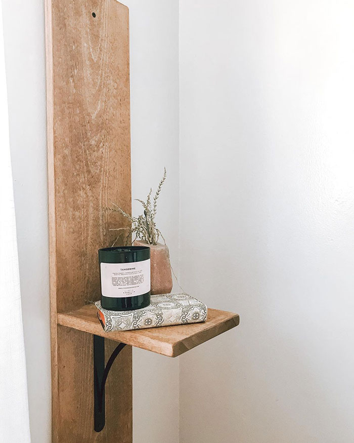 Floating nightstand with brackets mounted on wooden plank, styled with candle and vase in a minimalist bedroom corner.
