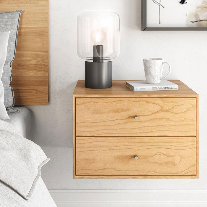 Floating nightstand with drawers in a modern bedroom setting featuring a lamp, book, and coffee mug on top.