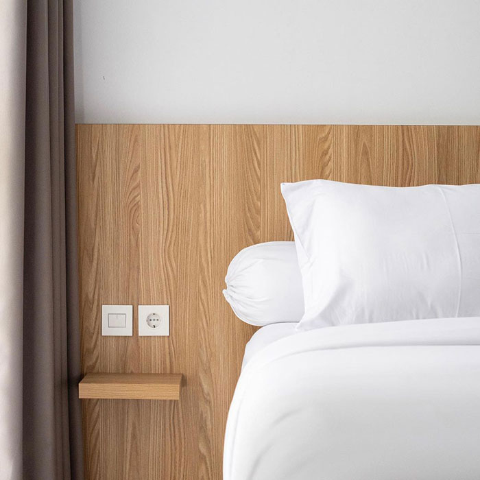 Floating nightstand connected to a wooden headboard in a modern bedroom with white bedding and neutral curtains.