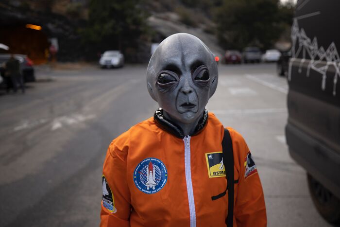 A person in an alien costume wearing an orange spacesuit on a road, evoking shower thoughts questions about extraterrestrials.