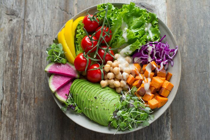 A colorful salad with lettuce, cherry tomatoes, avocado, chickpeas, and sweet potatoes, arranged in a bowl.