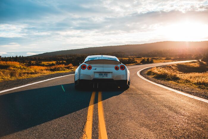 White car on a scenic road at sunset, evoking thoughts and questions about travel and exploration.