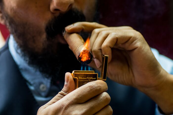 Man lighting a cigar with a lighter, contemplating deep thoughts.