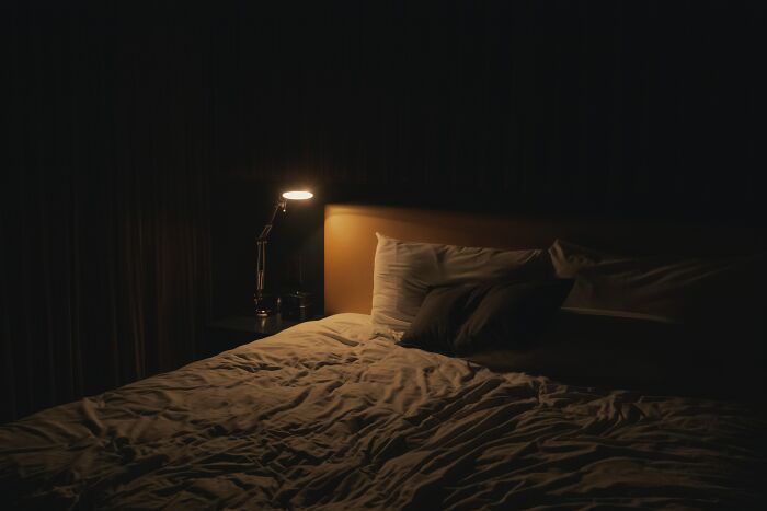 A dimly lit room with a cozy bed and a bedside lamp, evoking thoughtful shower reflections.