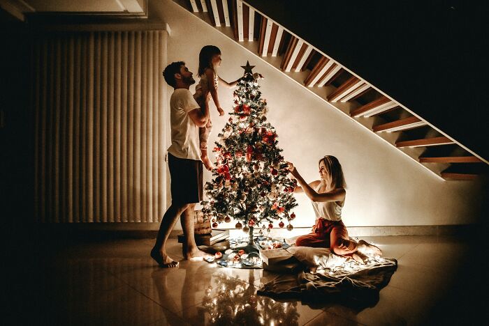 Family decorating a Christmas tree under staircase, evoking thoughts and questions about holiday traditions and togetherness.
