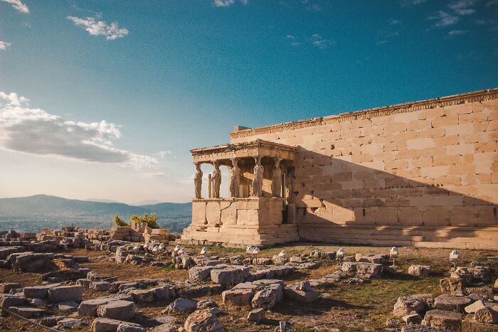 Ancient Greek ruins with statues under a clear blue sky, evoking reflection reminiscent of shower thoughts.