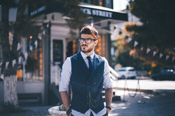A man in a vest and tie stands outside on a sunny day, embodying thoughtful style.
