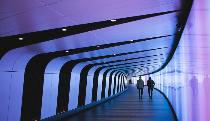 Two people walking through a futuristic tunnel, evoking shower thoughts with its abstract design.