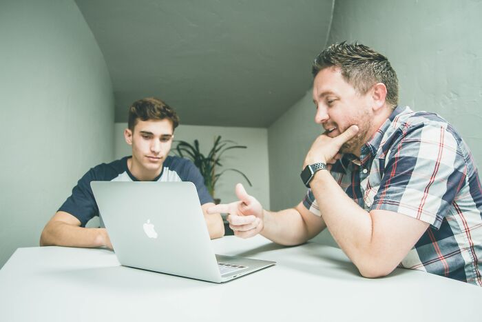 Two people engaged in a discussion at a table, focusing on shower thoughts questions over a laptop.
