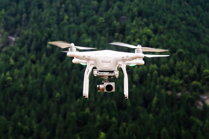A drone flying over a forest, capturing aerial views that spark shower thoughts.