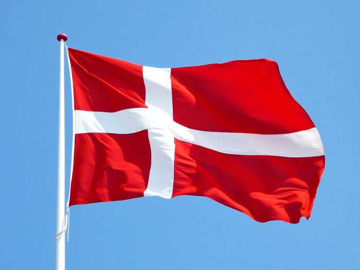 Danish flag waving against a clear blue sky, evoking cultural shower thoughts.
