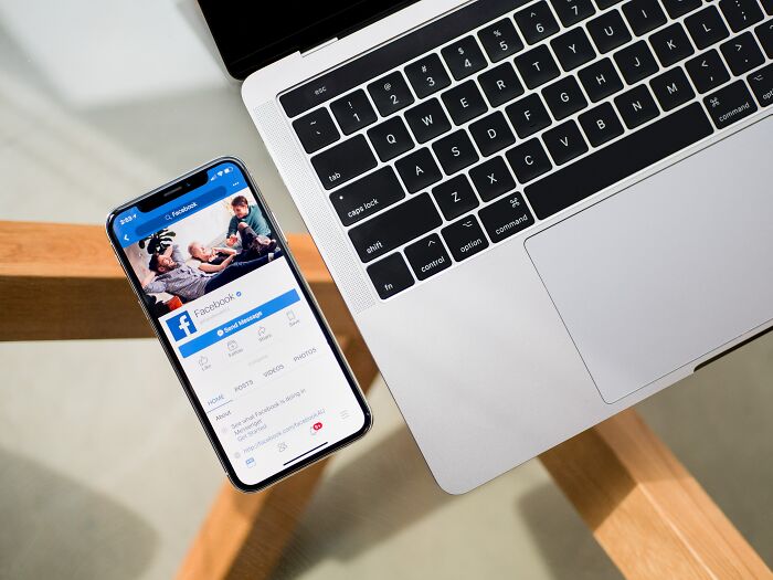 Smartphone displaying Facebook next to a laptop on a wooden desk, related to shower thoughts questions.