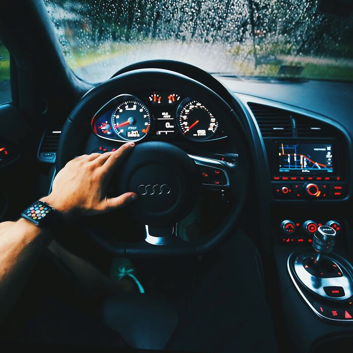 Inside a car during a rainy day, with a hand on the steering wheel, evoking shower thoughts questions.