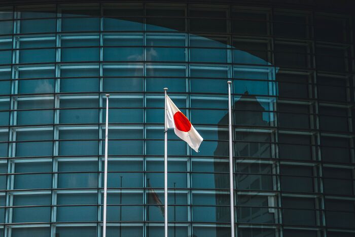 Japanese flag in front of a modern building, inspiring shower thoughts questions.