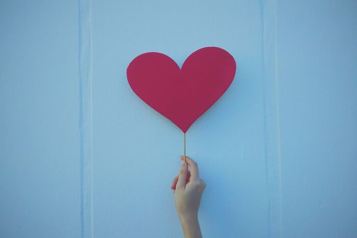 Hand holding a red heart-shaped cutout against a light blue background, symbolizing shower thoughts questions.