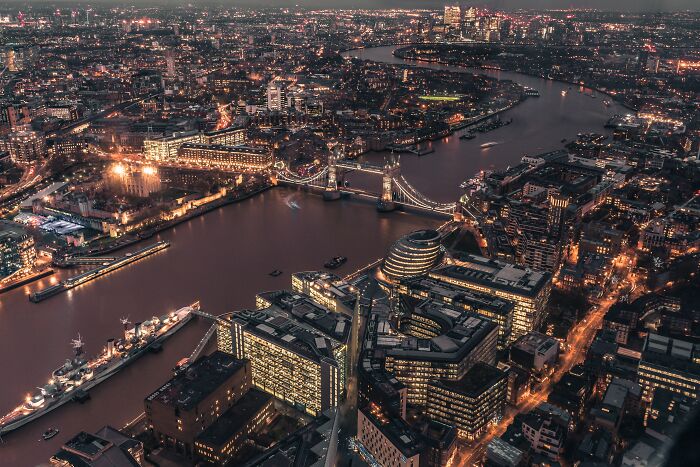 Aerial night view of a city with illuminated buildings and river, illustrating wealth and challenges in different countries.