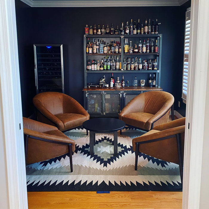 Small minimalist home bar with leather chairs and a black metal shelving unit filled with various liquor bottles. Small minimalist home bar with leather chairs and a black metal shelving unit filled with various liquor bottles.