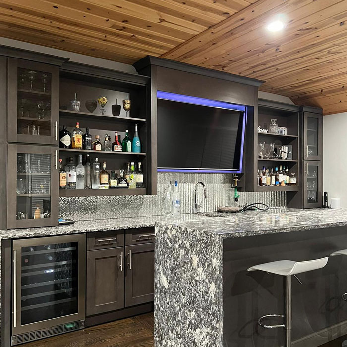 Marbled home bar island with dark cabinets, bar stools, and backlit shelving showcasing bottles and glassware. Marbled home bar island with dark cabinets, bar stools, and backlit shelving showcasing bottles and glassware.