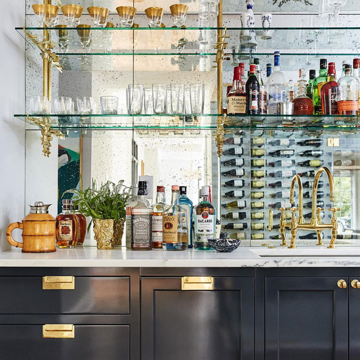 Home bar with mirrored backsplash, glass shelves holding liquor bottles and gold-accented fixtures for stylish happy hour. Home bar with mirrored backsplash, glass shelves holding liquor bottles and gold-accented fixtures for stylish happy hour.