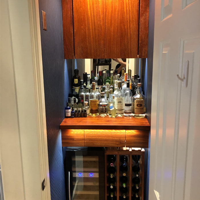 Small closet bar with wooden shelves, wine cooler, and assorted liquor bottles for creative home bar ideas. Small closet bar with wooden shelves, wine cooler, and assorted liquor bottles for creative home bar ideas.
