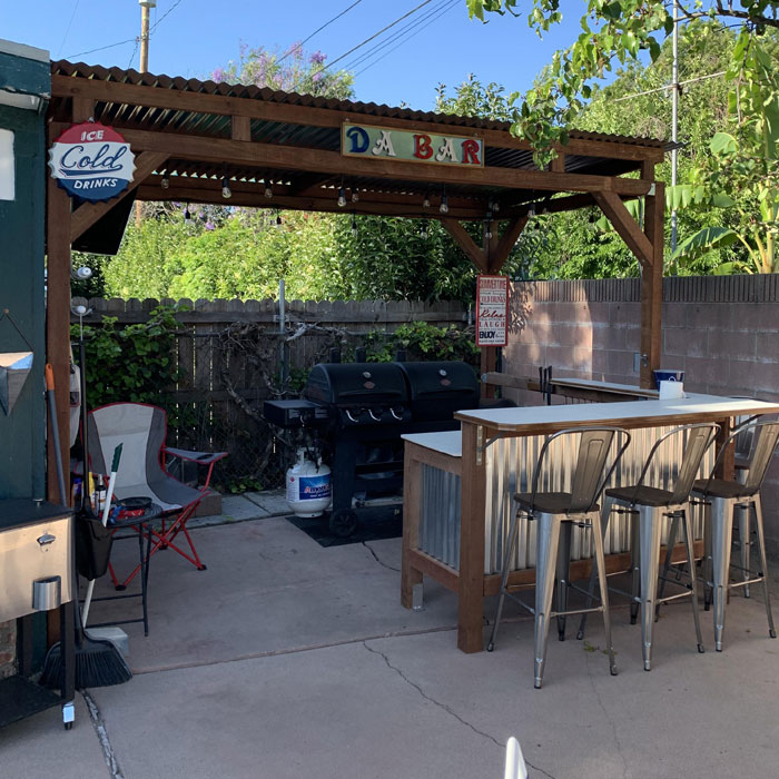 Outdoor deck home bar with metal stools, grill, and wood pergola creating a cozy space for happy hour gatherings. Outdoor deck home bar with metal stools, grill, and wood pergola creating a cozy space for happy hour gatherings.